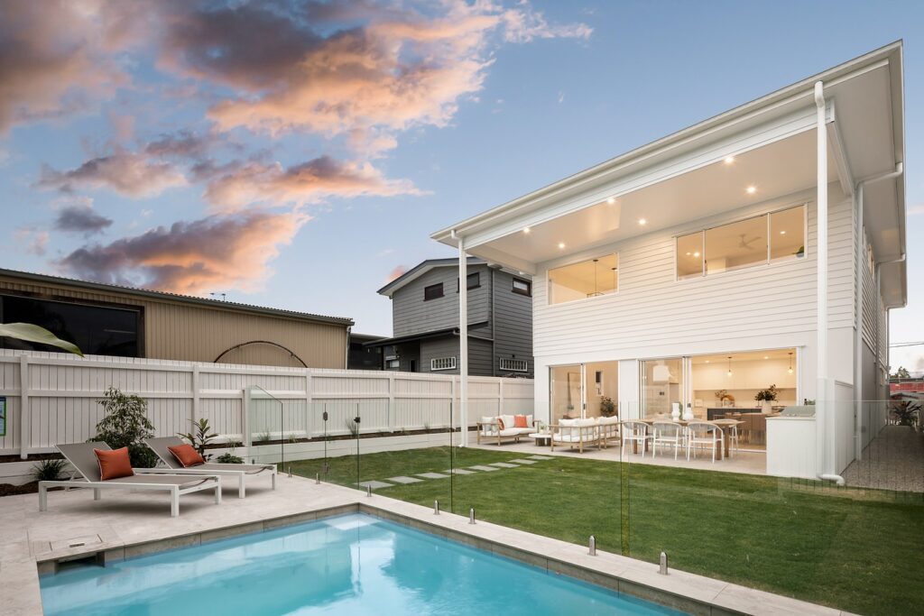 A spigot-fixed frameless glass pool fence seamlessly separating a backyard swimming pool from the lawn and outdoor dining area.